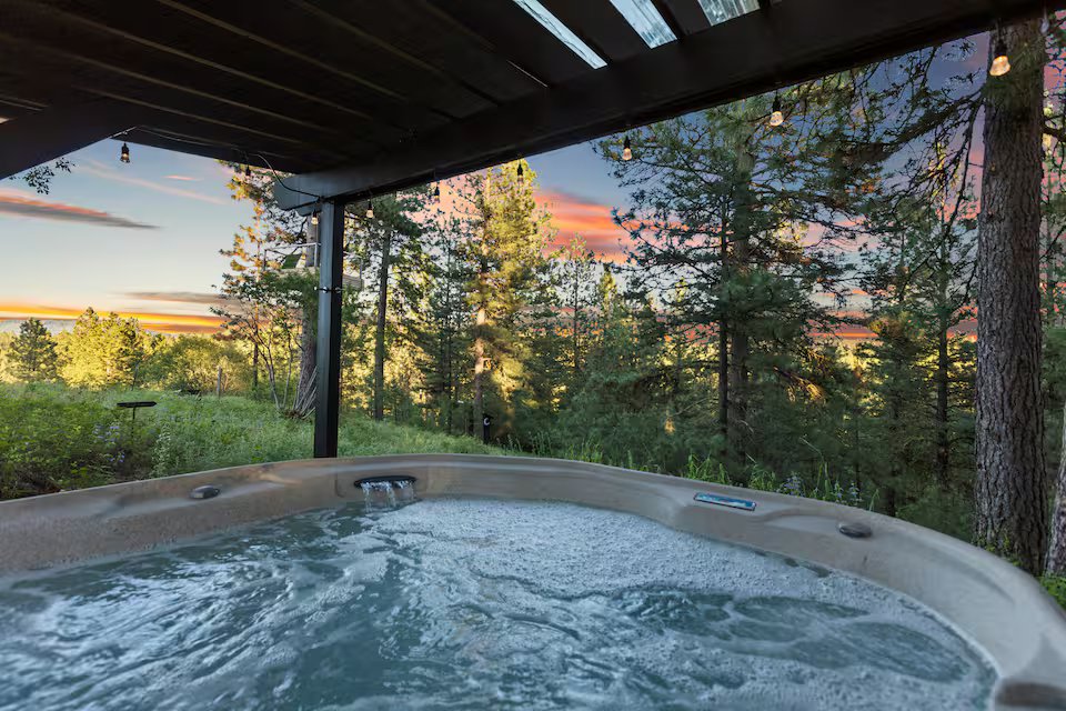 Hot tub with sunset glowing through pine trees at Banks Treehouse