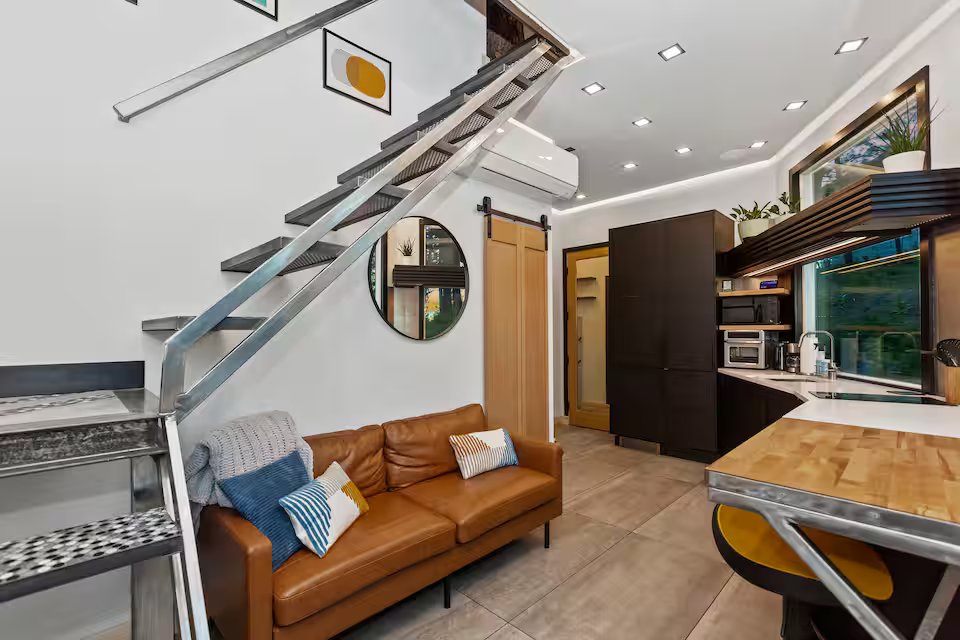 Living room with steel stairs, leather couch, and kitchen behind